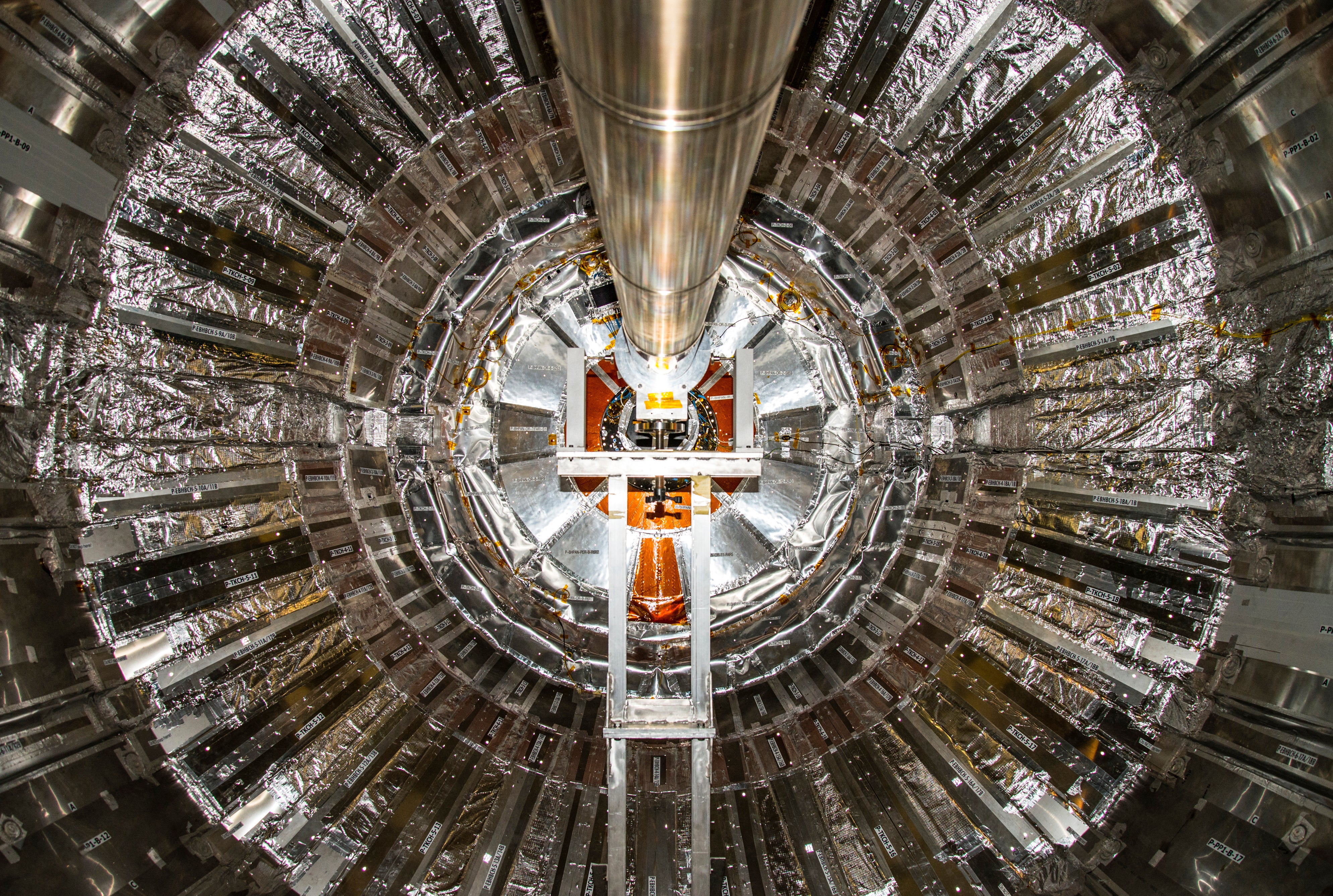 Innenansicht eines ringförmigen Teilchendetektors mit metallischen Segmenten und reflektierenden Oberflächen, zentral durchzogen von einem zylindrischen Element.