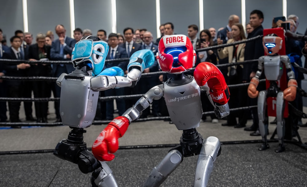 Zwei humanoide Roboter mit Boxhandschuhen und Schutzhelmen kämpfen in einem Boxring vor einem Publikum – Vorführung auf einer Technologiemesse