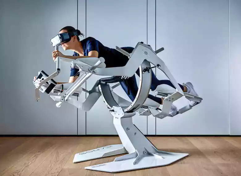 Person trägt VR-Headset und trainiert auf einem weißen, futuristischen Flugsimulator-Fitnessgerät in Bauchlage.