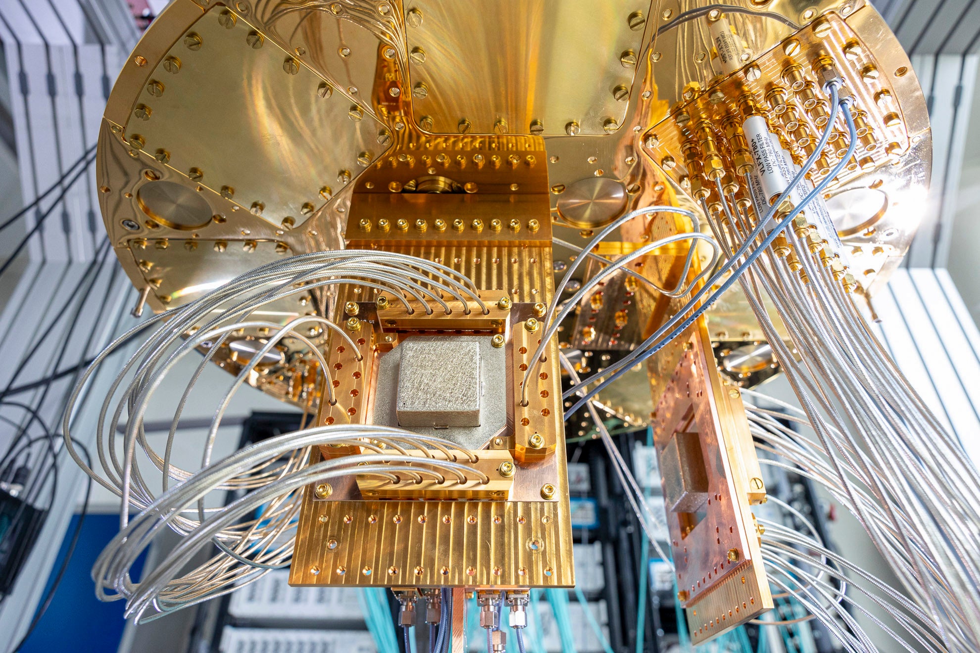 Detailaufnahme eines goldfarbenen Quantenprozessors mit zahlreichen koaxialen Leitungen und präzisen Metallkomponenten in Laborumgebung.