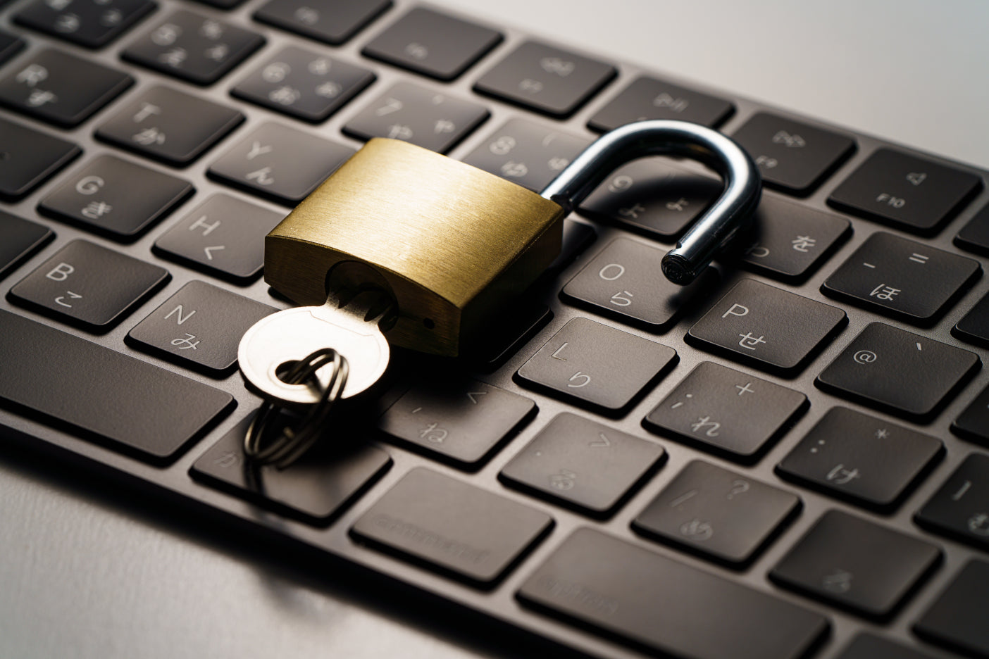 Aufgeschlossenes Messingschloss mit Schlüssel liegt auf einer Computer-Tastatur als Symbol für IT-Sicherheit.