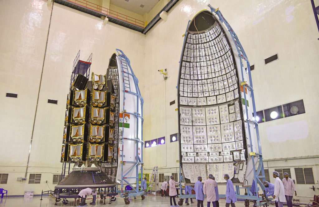 Techniker:innen in Schutzkleidung arbeiten an einer großen Raketenkapsel mit Dutzenden Satelliten im Inneren.