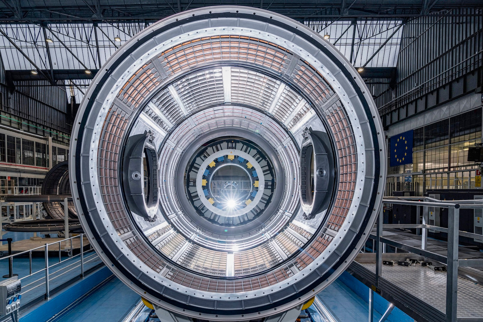 Blick in eine große, runde Hochtechnologie-Anlage mit konzentrischen Spulen in einer Industriehalle.