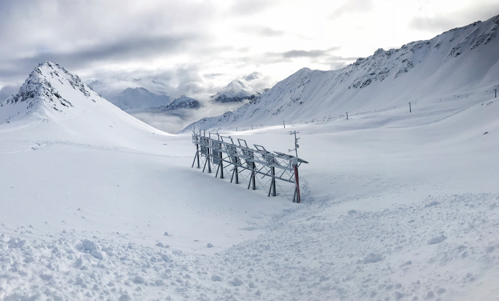 Schneebedeckte Berglandschaft mit technischer Messanlage auf Metallgestell, unter wolkenverhangenem Himmel.